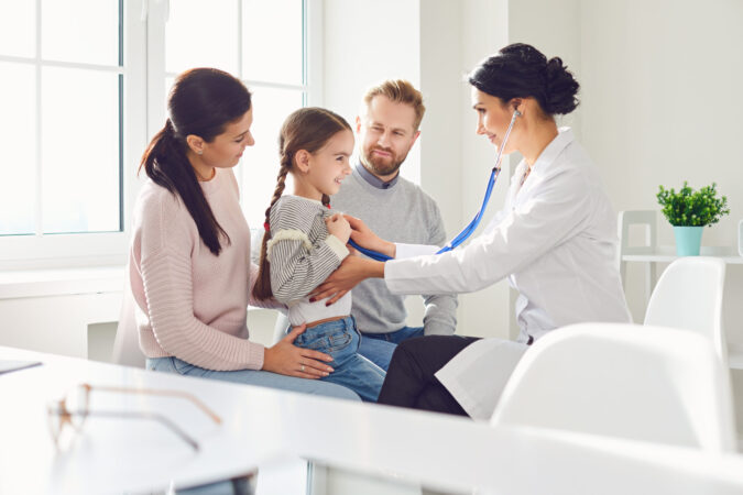 Happy family on a visit to the doctor in the office of a doctor. Woman family doctor sitting at the table with smiling family at the clinic.