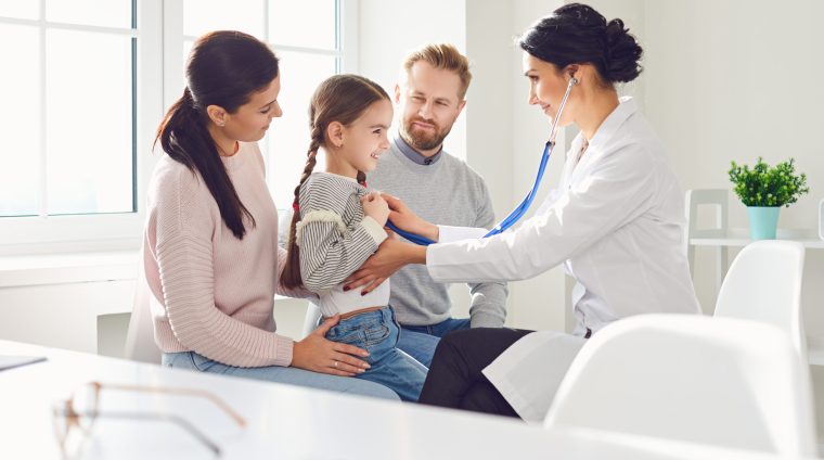 Happy family on a visit to the doctor in the office of a doctor. Happy family on a visit to the doctor in the office of a doctor. Woman family doctor sitting at the table with smiling family at the clinic.