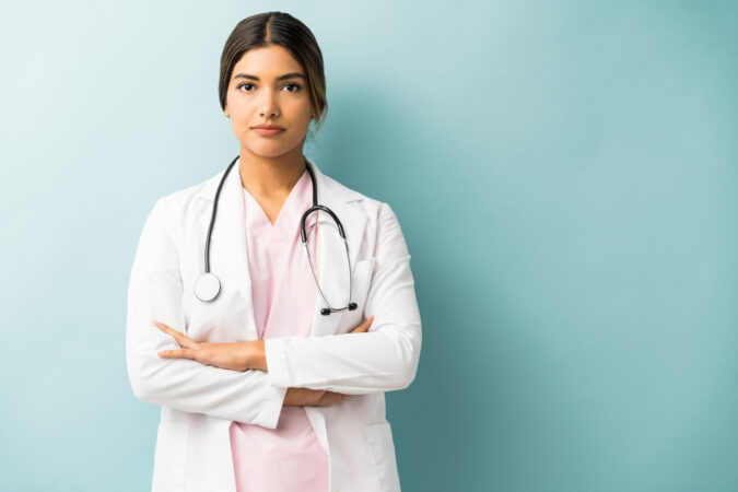 Attractive medical professional in uniform standing with arms crossed against isolated background