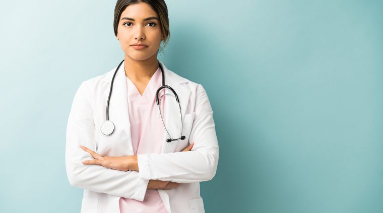 Doctor Wearing Lab Coat Standing Confidently In Studio Attractive medical professional in uniform standing with arms crossed against isolated background