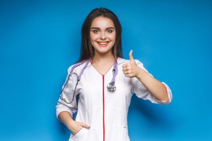 Gorgeous  young female doctor make okaysign, over blue background. Young medidcine.