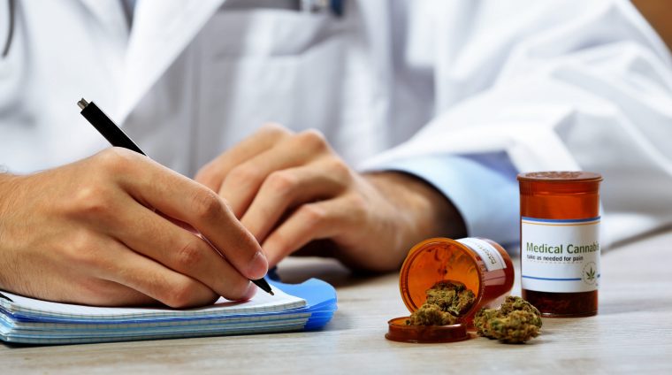 Doctor writing on prescription blank and bottle with medical cannabis on table close up